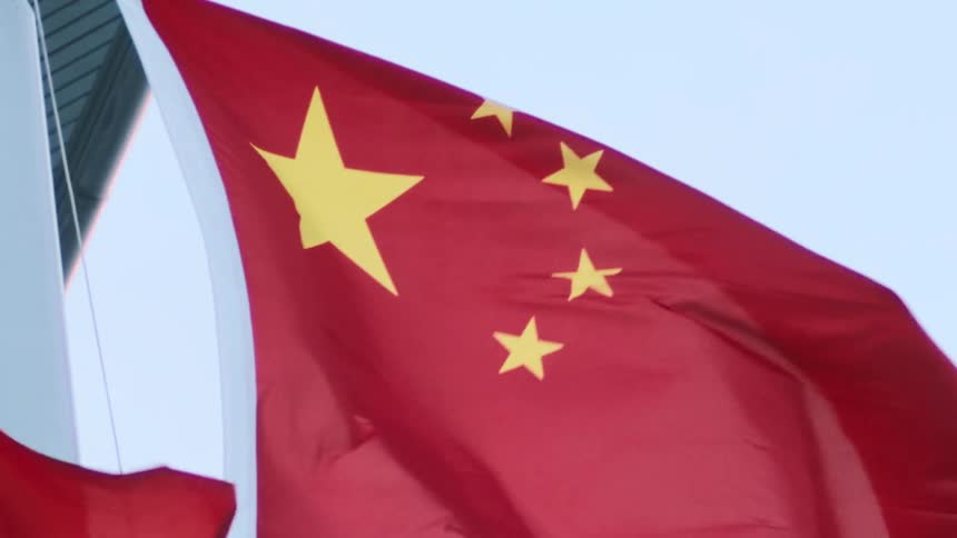 The video is a closeup shot of the red flag of the peoples republic of china with its large and four smaller yellow stars the flag is waving in the wind against a bright lightblue sky
