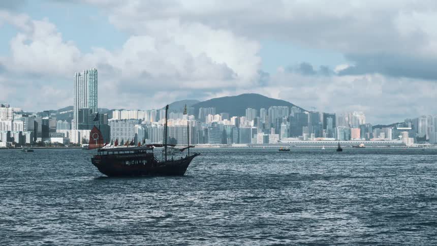 Traditional boat sails across the waters with hong kongs cityscape in the background