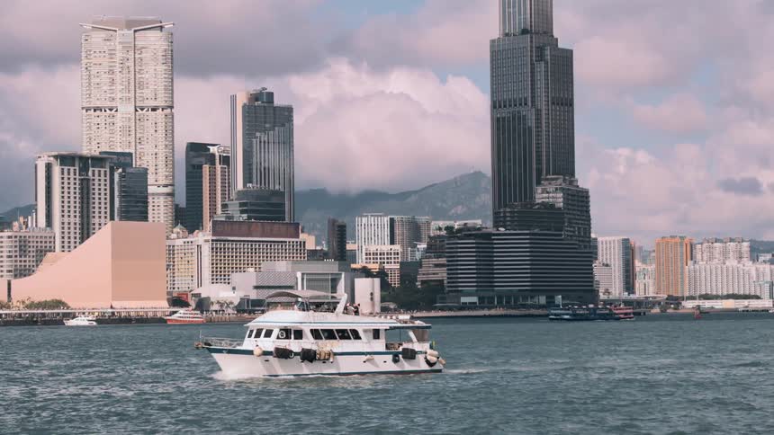 White boat sailing near skyscrapers under a partly cloudy sky