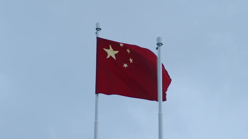 Two flagpoles stand side by side at sundownone hosts a chinese flag fluttering in the wind while the other remains empty