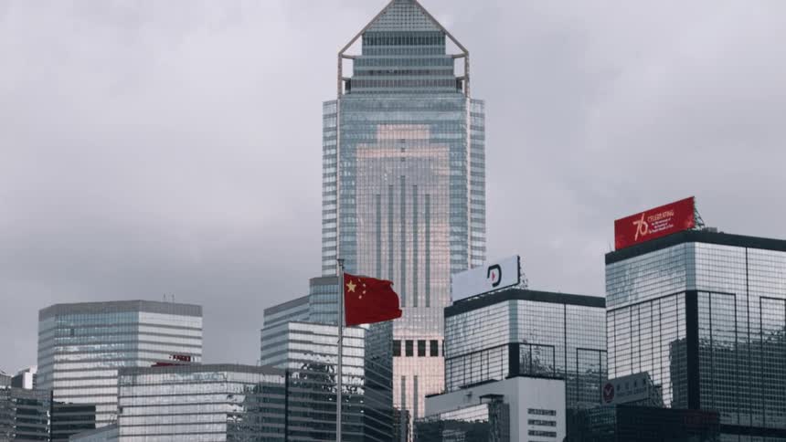 Mirrored buildings with the chinese flag waving under a cloudy sky