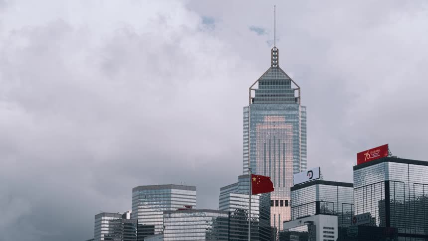Mirrored skyscrapers of hong kong with the chinese flag waving under a cloudy sky