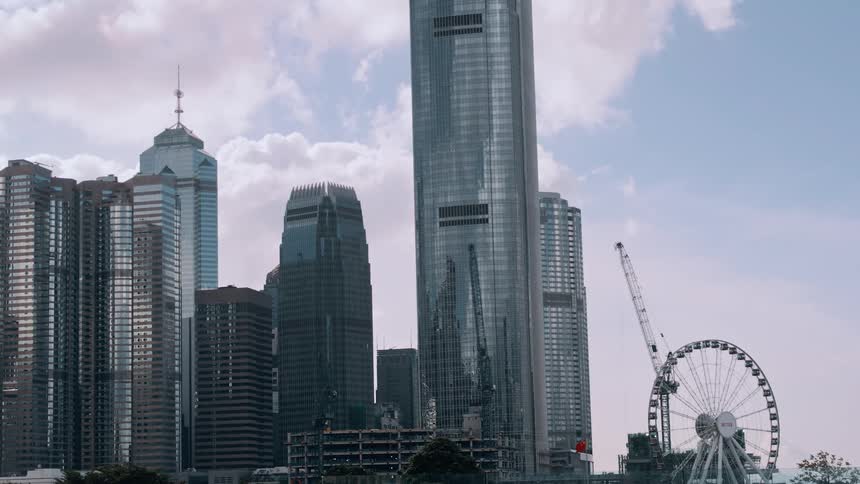 Modern skyscrapers beside a ferris wheel under a blue sky with light clouds