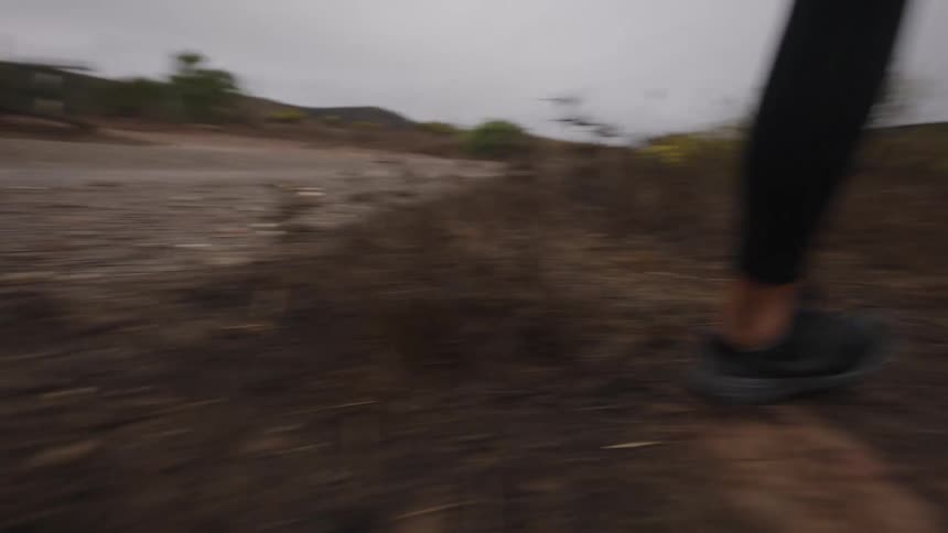 The video is a lowangle shot focusing on the legs of a person running down a rural gravel path the runner is wearing black athletic tights and black sneakers on a seemingly cloudy or overcast day