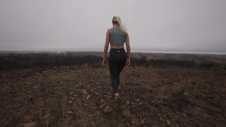 A woman in athletic wear walks up a rocky hill on an overcast day