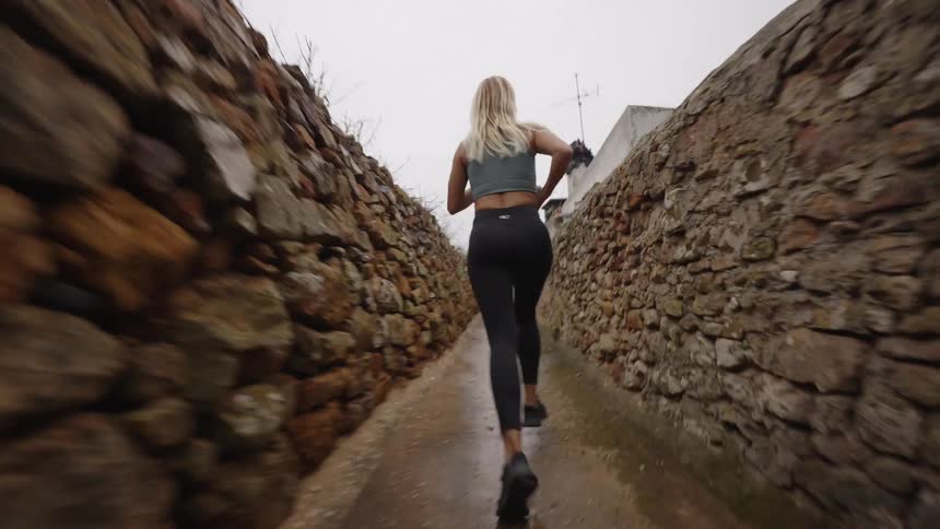 Woman running through a narrow stone pathway on a cloudy day