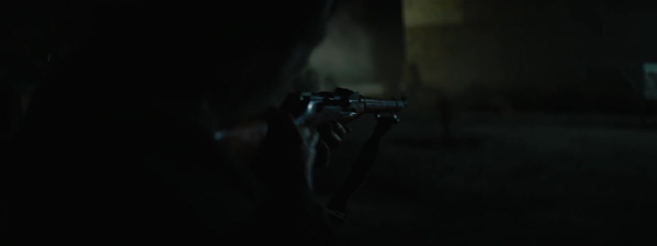A man holds and aims a gun in the dark