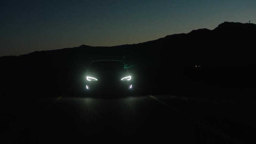 A car headlights come on as it drives the road at night