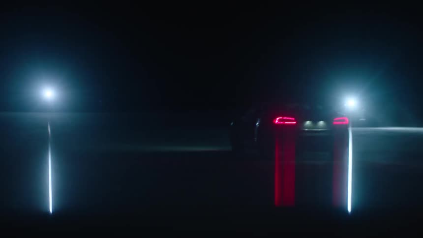 A car sitting in a lot at night with another car on the opposite end