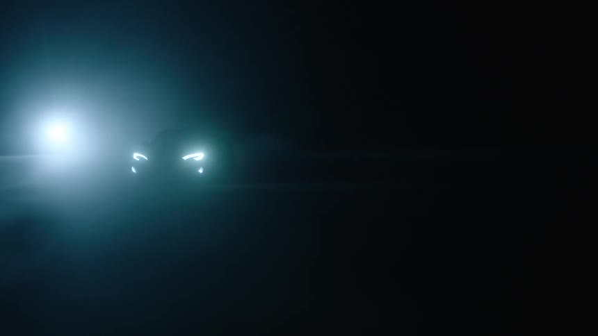 Car driving on pavement at night with a light shining in the background