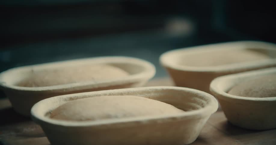 Bread doughs rising in proofing baskets on a wooden table