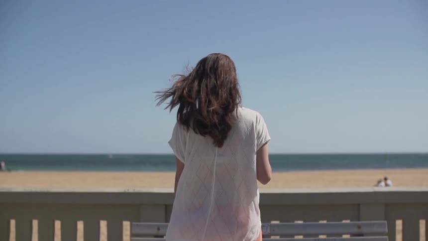 Woman walks towards a railing by the beach