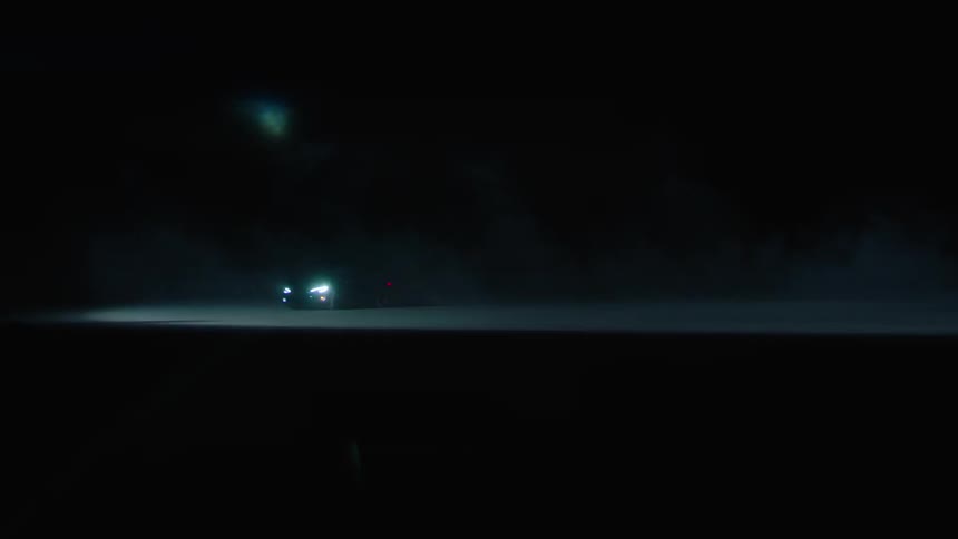 A car drives with its headlights on at night