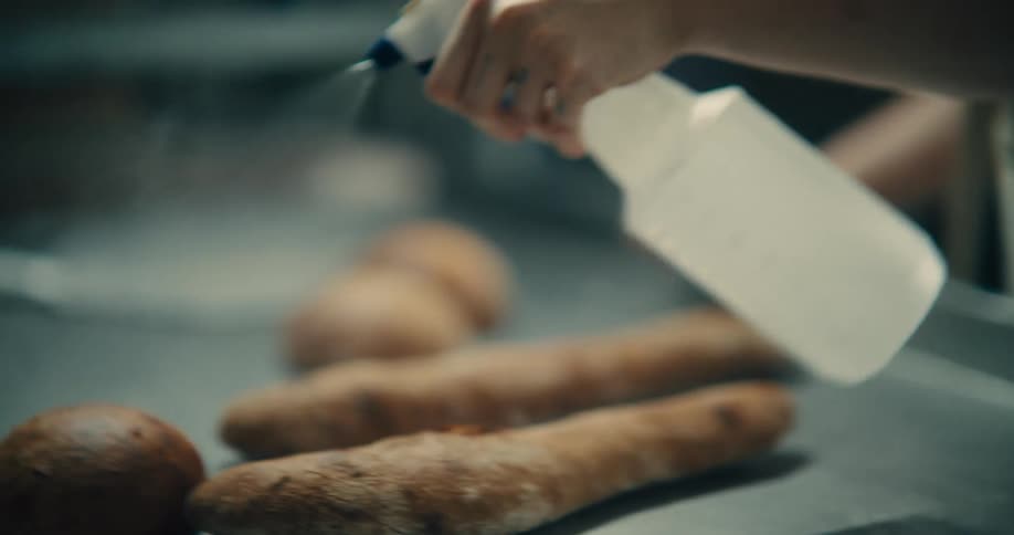 Close up of a woman spraying baked bread of various shapes with a liquid from a spray bottle