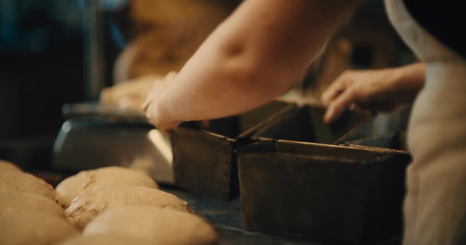 Close up of a young woman arranging metal baking containers for bread dough on a counter top