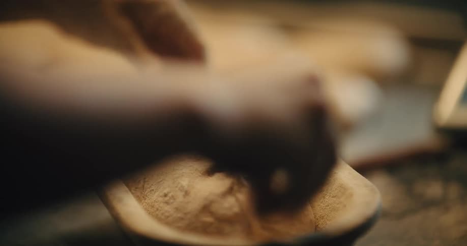 Hands shaping bread dough in a floured proofing basket