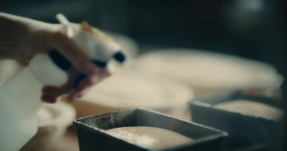 Person spraying water over bread dough in metal pans