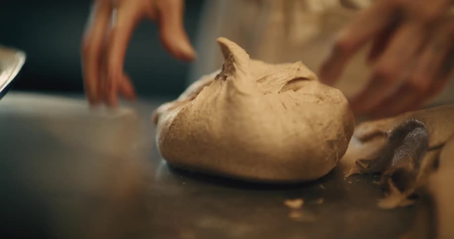 Close up of a woman kneading baking dough with her hands on a counter top