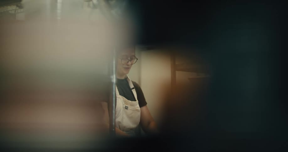 A smiling female baker with glasses and an apron working in a bakery