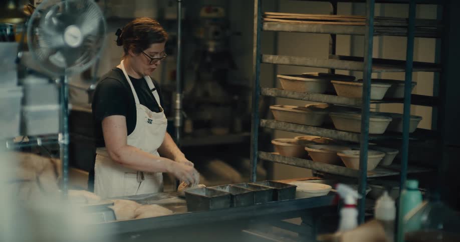 A young woman kneading baking dough on a table in a bakery