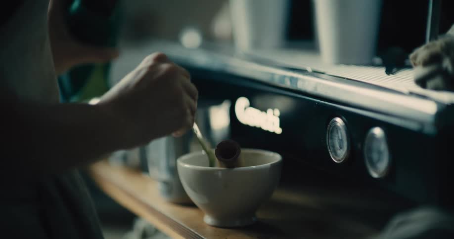 A barista spoons match powder into a bowl next to a commercial expresso machine