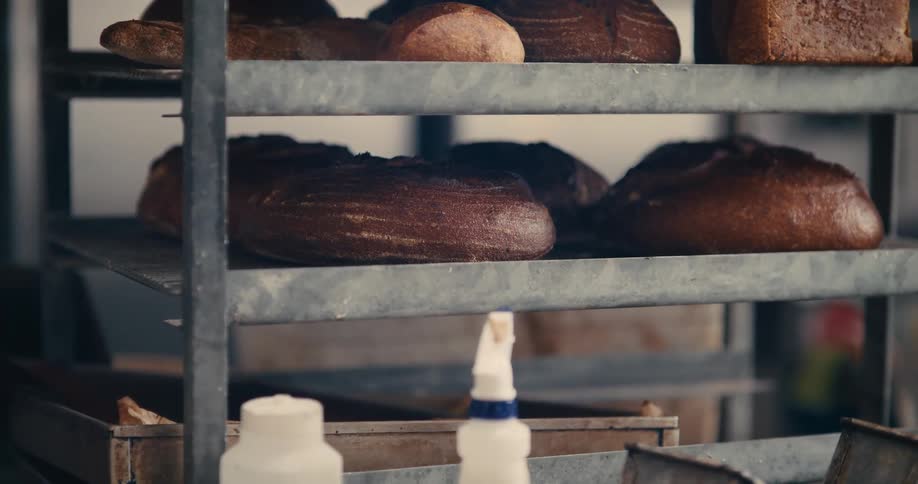 Close up of a female worker arranging baked bread on a metal rack in a bakery during daytime