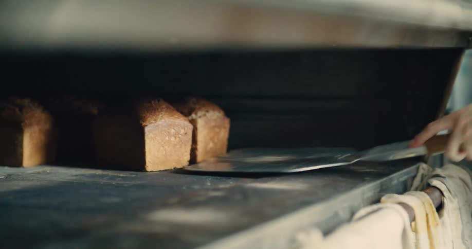 Baker taking golden bread out of the oven with a metal shovel