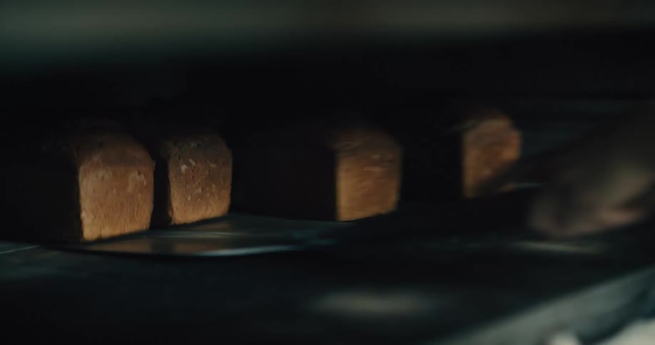 Close up of a baker putting loaves into an oven