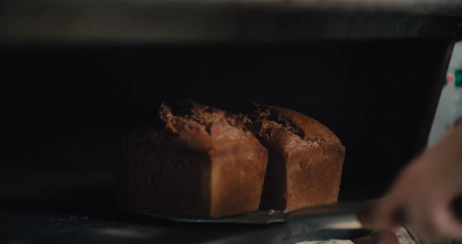 A baker removes two freshly baked loaves of bread from an oven in a bakery