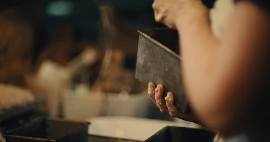 A baker's hands brushing butter on the inside of a loaf tin.