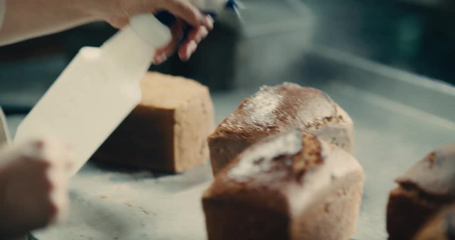 A baker sprays loaves with a glze