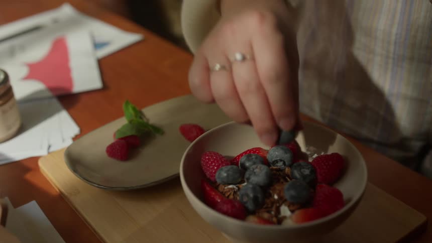 Close up of a woman garnishing a bowl of cereal with fruits and vegetables