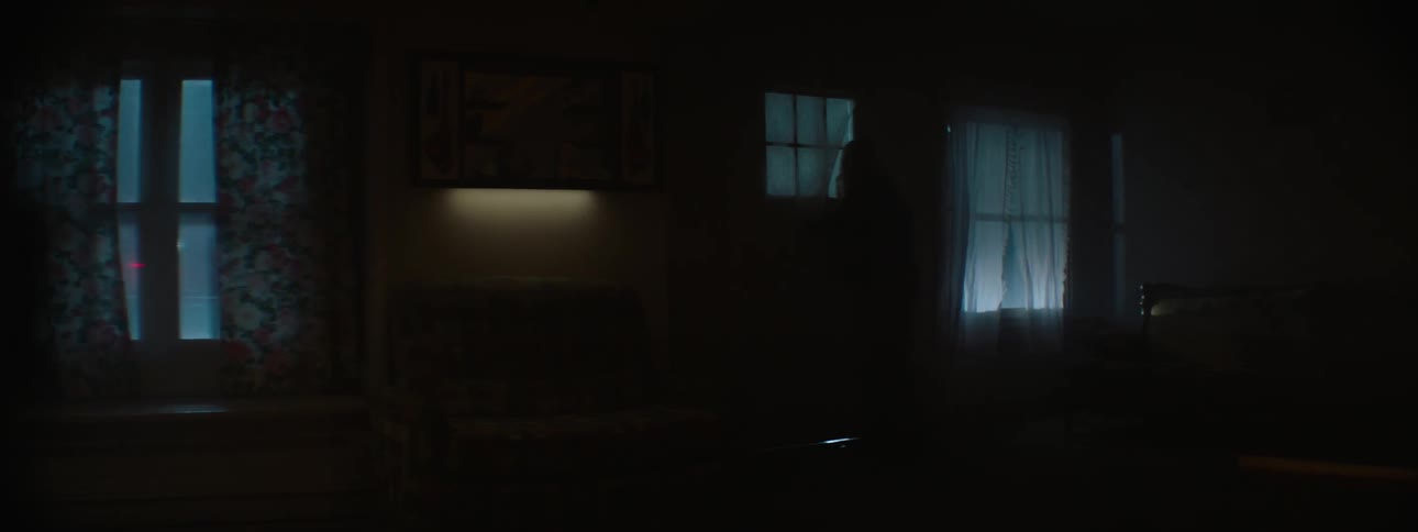 A woman looks out the window and the door at lights shining
