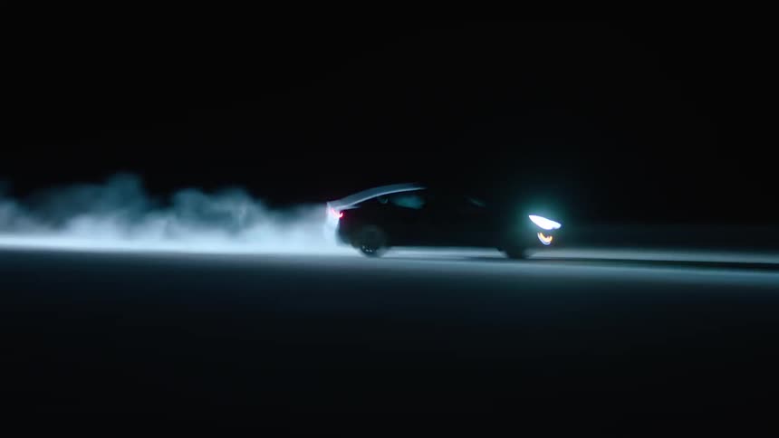 A car drives with its headlights on at night