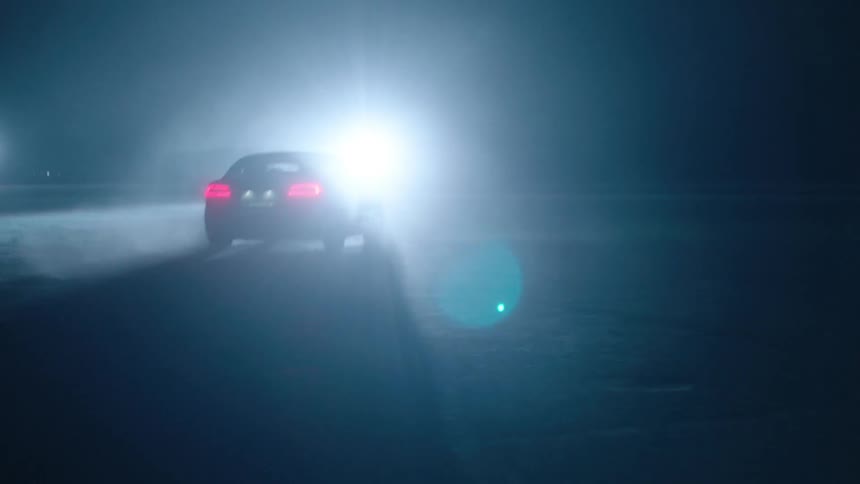 A car zigzags towards a bright light at night