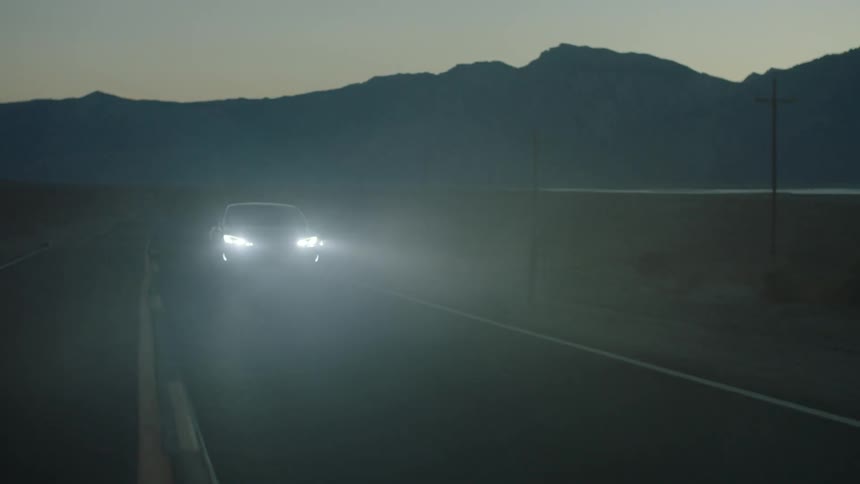 A car is driving down a road at dawn