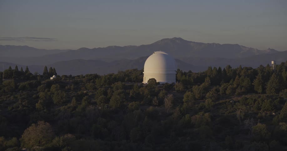 White observatory surrounded by forest with mountains in the background under golden light