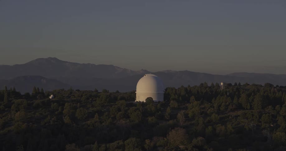 White observatory amid a forest with mountains in the background at dusk