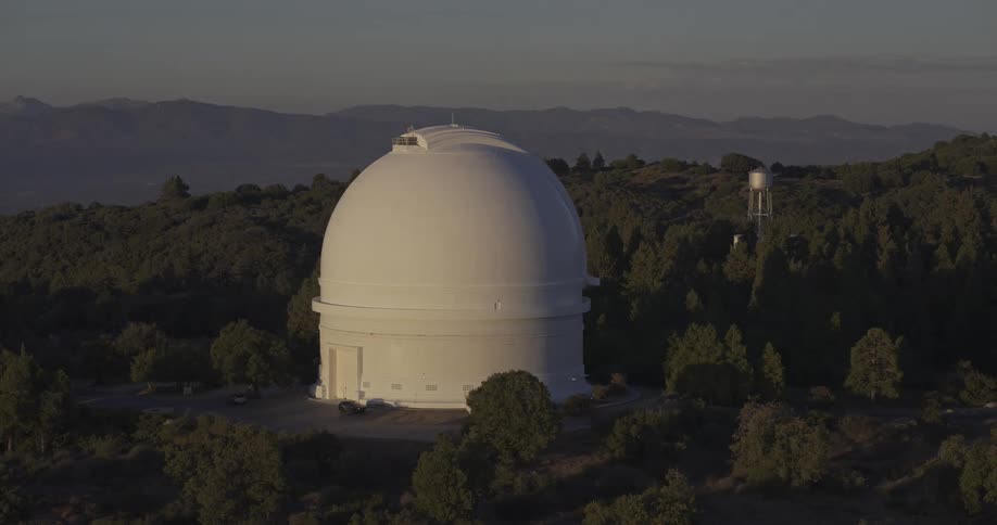 White observatory surrounded by trees and mountains under soft evening light