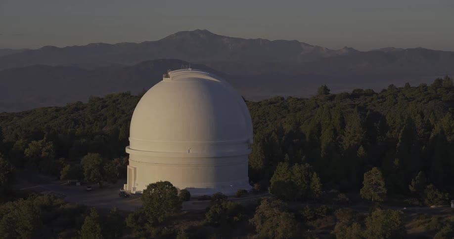 White observatory surrounded by trees with mountains in the background under soft light