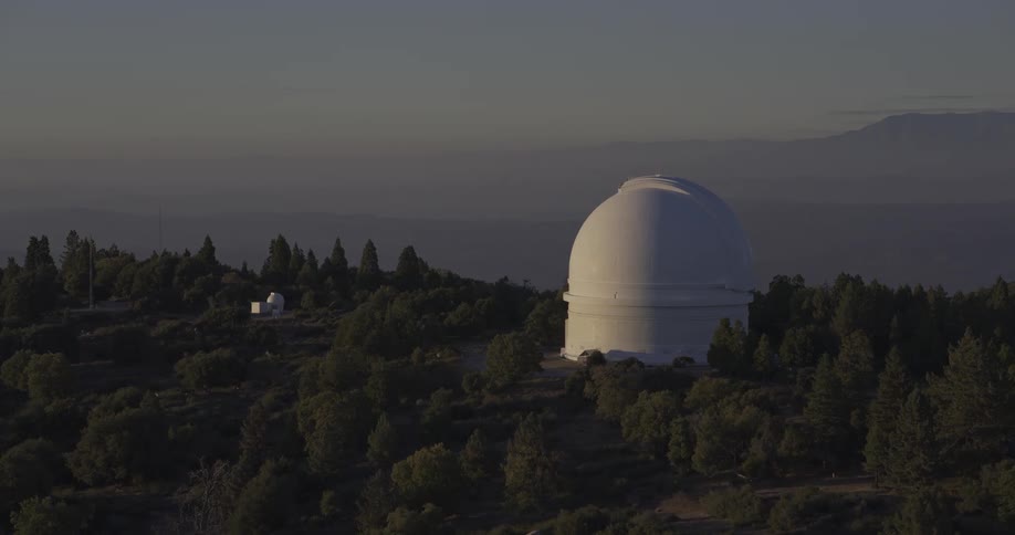 A large observatory dome sits atop a forested mountain at twilight