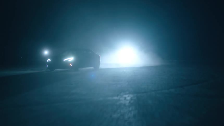 A car zigzags in front of a bright light at night