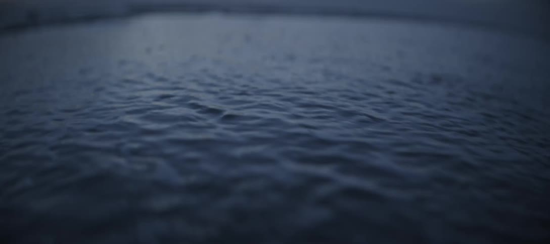 A close view of small ocean waves rolling onto a sandy beach at dusk or dawn with dark blue water and a subtle foamy white wave crest