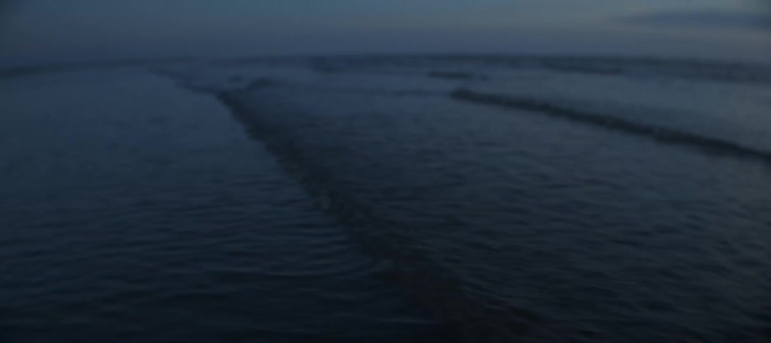 A slow wide view of dark blue ocean waves rolling in multiple lines onto the beach under a hazy dim sky at either dusk or dawn