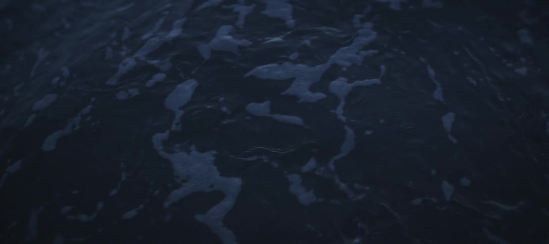 A close dark view of the ocean surface shows deep blue water with white foam from breaking waves quickly dissipating and bubbling in an abstract pattern