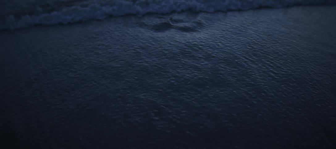 Dark gentle waves lap onto a sandy shore at twilight