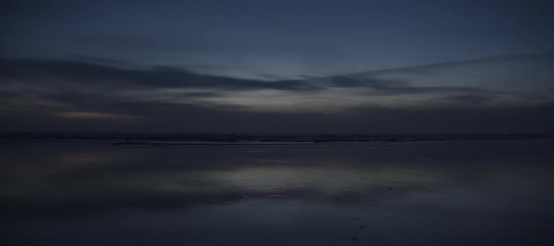 Dark sky reflected on the calm waters of a beach at dusk