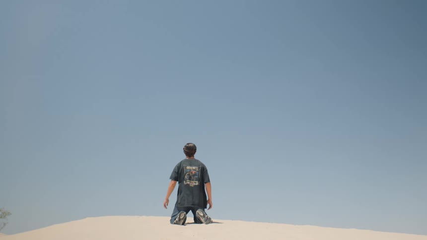 A man suddenly drops to his knees on a desert hill under the blazing midday sun his posture tense and his expression filled with frustration as the heat radiates across the barren landscape