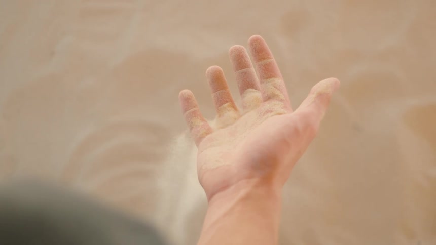 The video clip is a closeup overhead shot of a hand sifting and playing with fine lightcolored sand or dirt the surface is smooth and tan filling the frame while the fingers scoop and let the material trickle back down