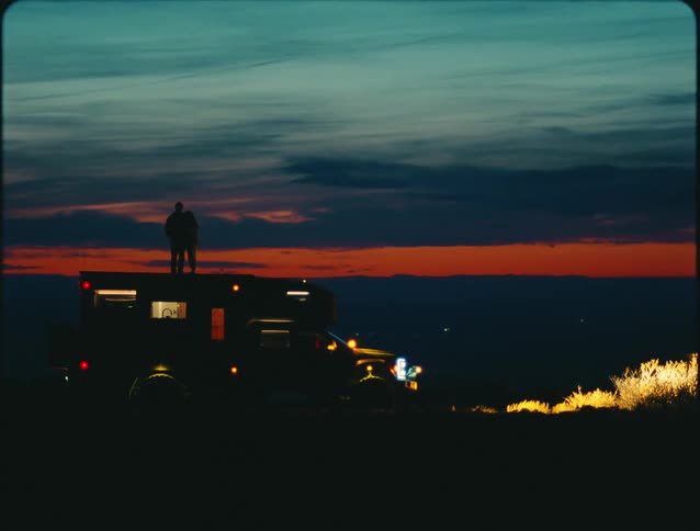Two people stand on their recreational vehicle and watch the sunset